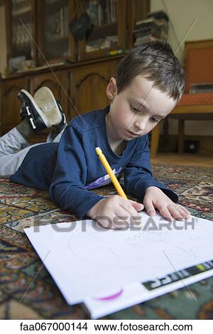 Boy lying on floor, drawing on paper with pencil View Large Photo Image Picture - Boy lying on floor, drawing on paper with pencil. Fotosearch