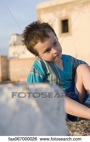 Boy sitting on the ground, looking away in thought View Large Photo Image Stock Photograph - Boy sitting on the ground, looking away in thought. Fotosearch