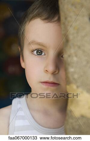 Stock Image - Little boy behind tree trunk, portrait. Fotosearch