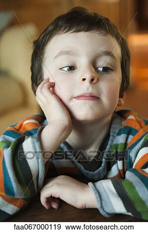 Stock Photo - Little boy sitting with hand under chin, looking away in thought. Fotosearch
