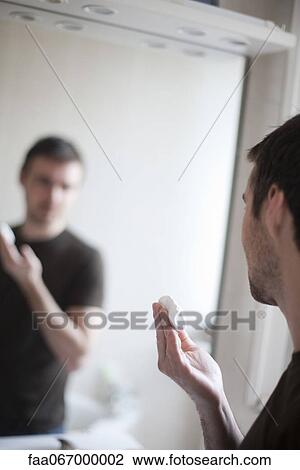 Stock Image - Man looking at self in mirror, shaving cream in hand. Fotosearch