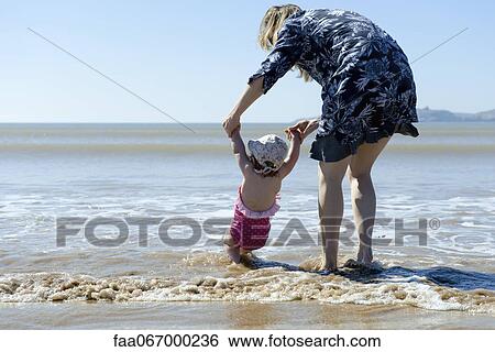 Mother and baby daughter walking in surf at the beach, rear view View Large Photo Image Stock Photograph - Mother and baby daughter walking in surf at the beach, rear view. Fotosearch