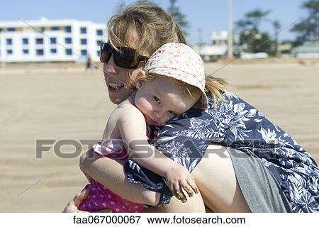 Stock Photo - Mother embracing baby daughter at the beach. Fotosearch