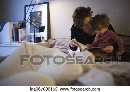 Stock Image - Mother holding toddler son on lap, reading bedtime story in bed. Fotosearch