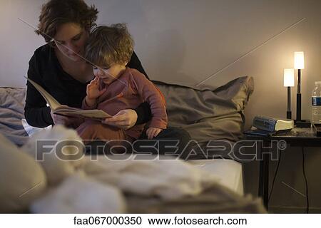 Stock Image - Mother holding toddler son on lap, reading bedtime story in bed. Fotosearch