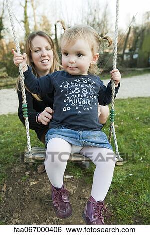 Mother pushing toddler girl on swing View Large Photo Image Stock Photograph - Mother pushing toddler girl on swing. Fotosearch
