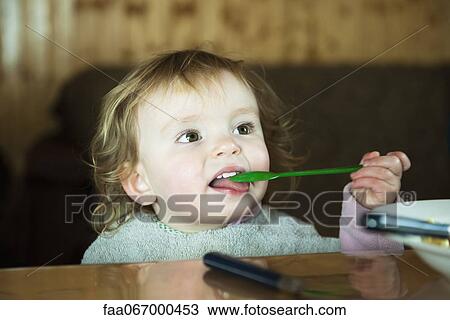 Stock Image - Toddler girl feeding herself with spoon. Fotosearch
