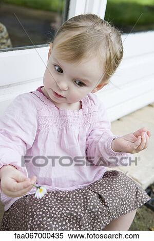 Stock Photography - Toddler girl holding flower, looking down curiously, portrait. Fotosearch