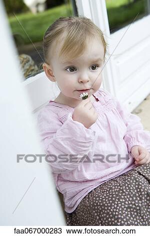 Stock Image - Toddler girl holding flower, portrait. Fotosearch