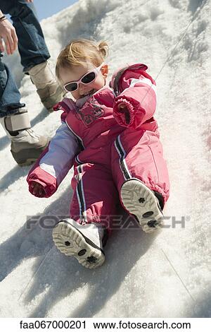 Stock Image - Toddler girl in snow-suit sitting on snow. Fotosearch