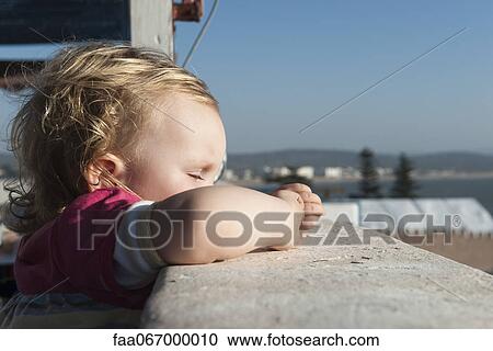 Stock Image - Toddler girl leaning against side of balcony with eyes closed. Fotosearch
