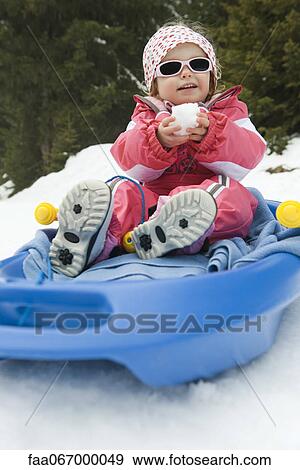 Stock Photo - Toddler girl on sled, snowball in hands. Fotosearch