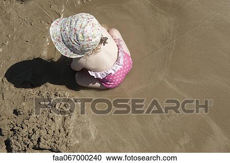 Stock Image - Toddler girl playing in sand at the beach. Fotosearch