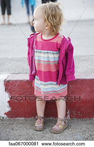 Stock Image - Toddler girl standing on sidewalk, looking over her shoulder. Fotosearch