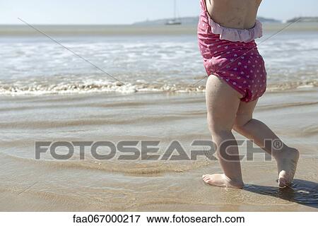 Stock Photo - Toddler girl walking in surf at the beach, low section. Fotosearch