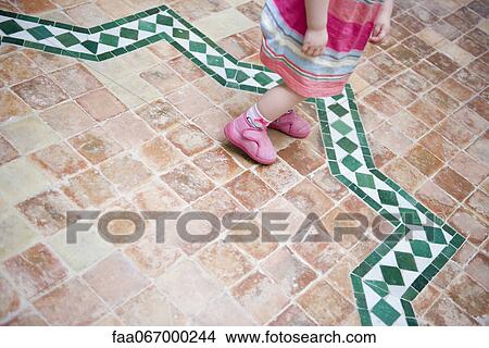 Picture - Toddler girl walking on tiled patio, low section. Fotosearch
