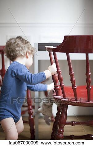 Stock Photo - Toddler standing by chair, side view. Fotosearch