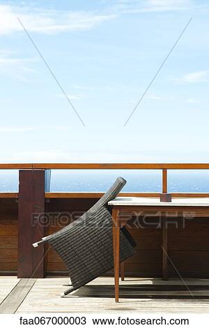 Stock Image - Wicker chair leaning against table on deck. Fotosearch