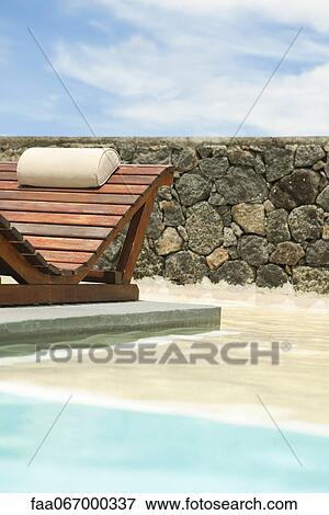 Stock Photo - Wooden lounge chair in pool. Fotosearch