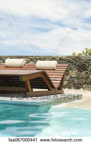 Stock Image - Wooden lounge chairs in pool. Fotosearch