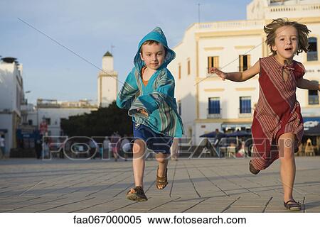 Stock Photography - Young siblings running together on sidewalk. Fotosearch