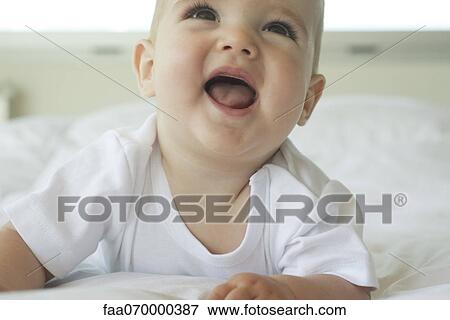 Stock Photo - Baby lying on bed, looking up with open mouth. Fotosearch
