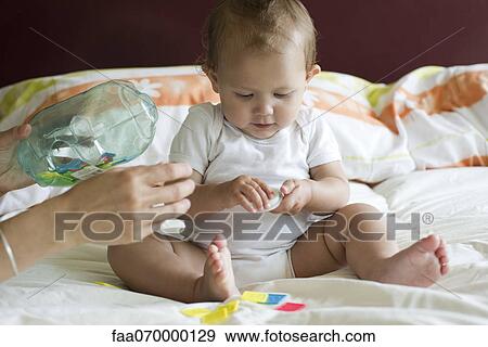 Baby sitting on bed, playing with toy View Large Photo Image Stock Photo - Baby sitting on bed, playing with toy. Fotosearch