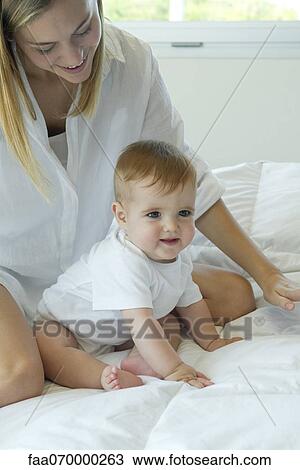 Baby sitting on bed with mother View Large Photo Image Stock Image - Baby sitting on bed with mother. Fotosearch