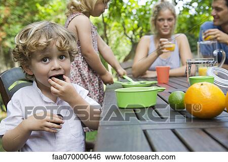 Boy enjoying outdoor snack with his family View Large Photo Image Stock Photograph - Boy enjoying outdoor snack with his family. Fotosearch