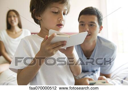 Boy reading book as parents watch in background View Large Photo Image Stock Image - Boy reading book as parents watch in background. Fotosearch