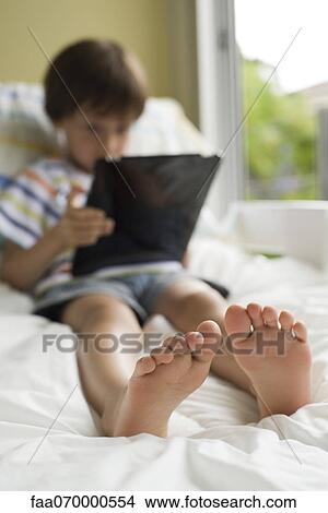 Boy relaxing on bed with digital tablet View Large Photo Image Picture - Boy relaxing on bed with digital tablet. Fotosearch