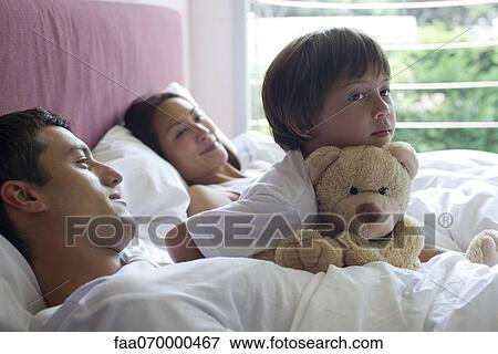 Boy sitting in bed with his parents and his teddy bear View Large Photo Image Stock Photo - Boy sitting in bed with his parents and his teddy bear. Fotosearch