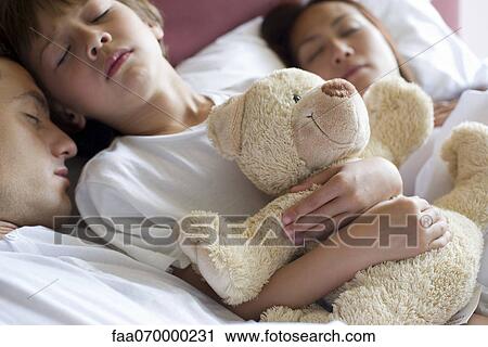 Boy sleeping in bed with his parents, holding teddy bear View Large Photo Image Stock Image - Boy sleeping in bed with his parents, holding teddy bear. Fotosearch