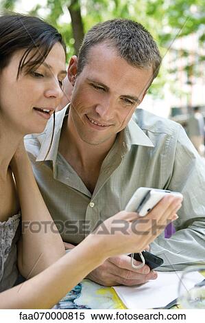 Couple looking at cell phone together outdoors View Large Photo Image Stock Photography - Couple looking at cell phone together outdoors. Fotosearch
