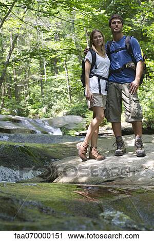 Stock Image - Couple standing by stream in woods. Fotosearch