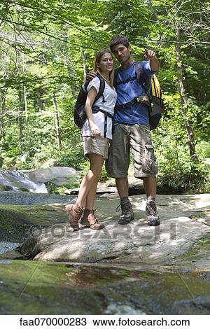 Stock Image - Couple standing by stream in woods. Fotosearch