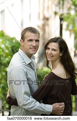 Stock Photograph - Couple together outdoors, smiling over shoulders at camera. Fotosearch