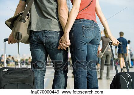 Stock Photo - Couple walking outdoors with rolling luggage. Fotosearch