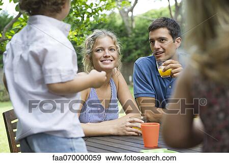 Family relaxing together at outdoor table View Large Photo Image Stock Photo - Family relaxing together at outdoor table. Fotosearch