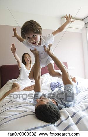 Family together on bed, father lifting son in the air View Large Photo Image Stock Image - Family together on bed, father lifting son in the air. Fotosearch