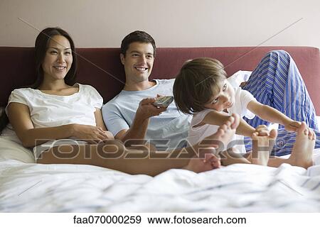 Stock Photo - Family watching TV together in bed. Fotosearch