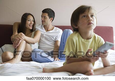 Stock Image - Family watching TV together on bed. Fotosearch