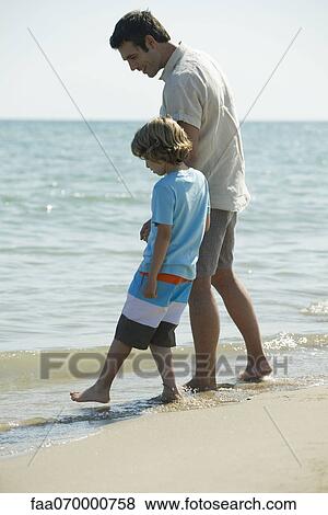 Father and son walking in surf at the beach View Large Photo Image Stock Photo - Father and son walking in surf at the beach. Fotosearch