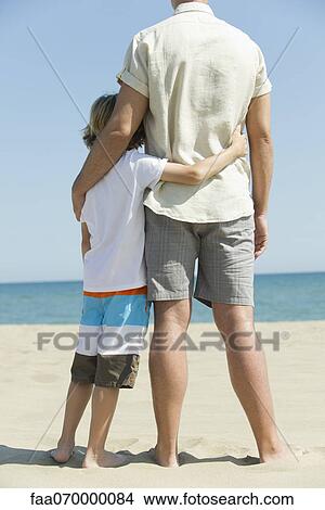 Father and young son standing together at the beach, rear view View Large Photo Image Picture - Father and young son standing together at the beach, rear view. Fotosearch