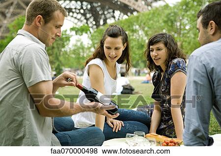 Friends enjoying picnic outdoors, admiring bottle of wine View Large Photo Image Stock Photo - Friends enjoying picnic outdoors, admiring bottle of wine. Fotosearch