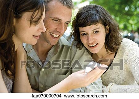 Friends looking at cell phone outdoors View Large Photo Image Picture - Friends looking at cell phone outdoors. Fotosearch