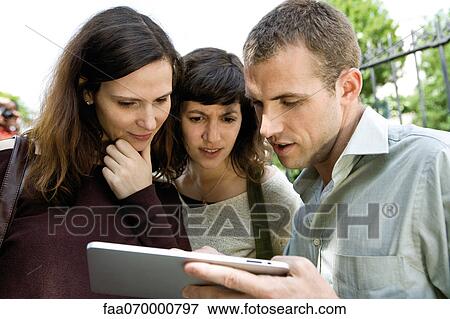 Friends looking at digital tablet outdoors View Large Photo Image Stock Photo - Friends looking at digital tablet outdoors. Fotosearch