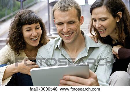 Stock Photo - Friends using digital tablet outdoors. Fotosearch
