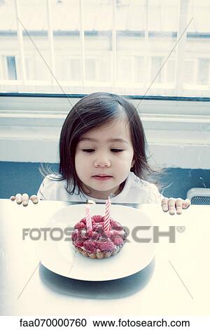 Stock Image - Little girl blowing out candles on birthday cake. Fotosearch
