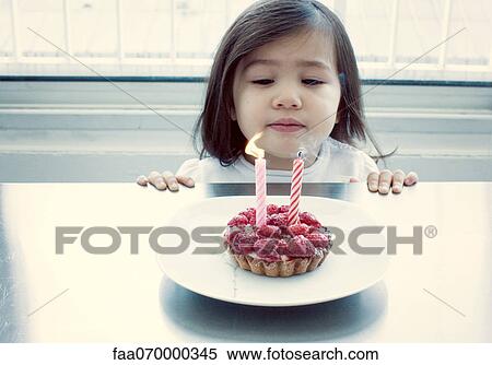 Stock Photography - Little girl blowing out candles on birthday cake. Fotosearch